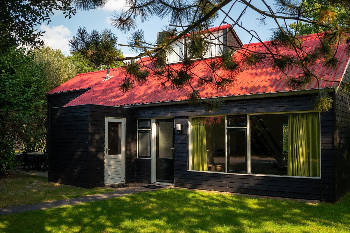 Une maison en bois à deux étages, avec un toit rouge, de grandes fenêtres et une porte.