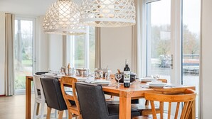 A dining area with a wooden table set for six, surrounded by chairs, and two white pendant lights above. - Summio Waterpark De Bloemert (Midlaren)