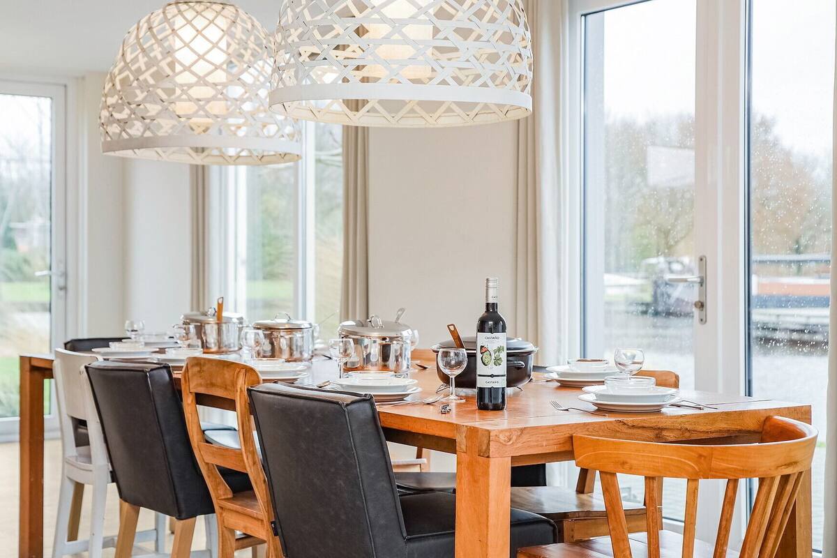 Un coin repas avec une table en bois dressée pour six personnes, entourée de chaises, et deux lampes suspendues blanches au-dessus.