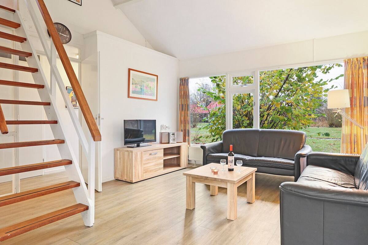 Un salon avec un escalier en bois, une télévision, un canapé, une table basse et une fenêtre donnant sur des arbres.