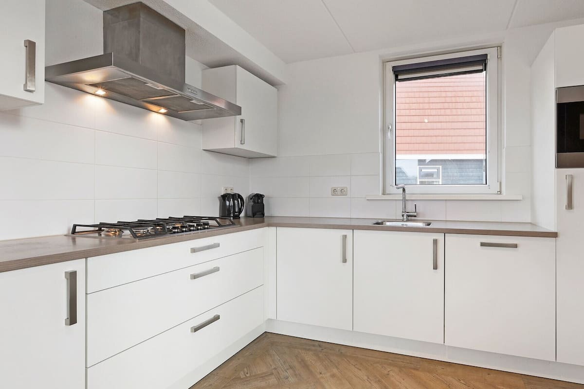 Une cuisine moderne avec des meubles blancs, une cuisinière à gaz, un four à micro-ondes et une fenêtre équipée de stores.