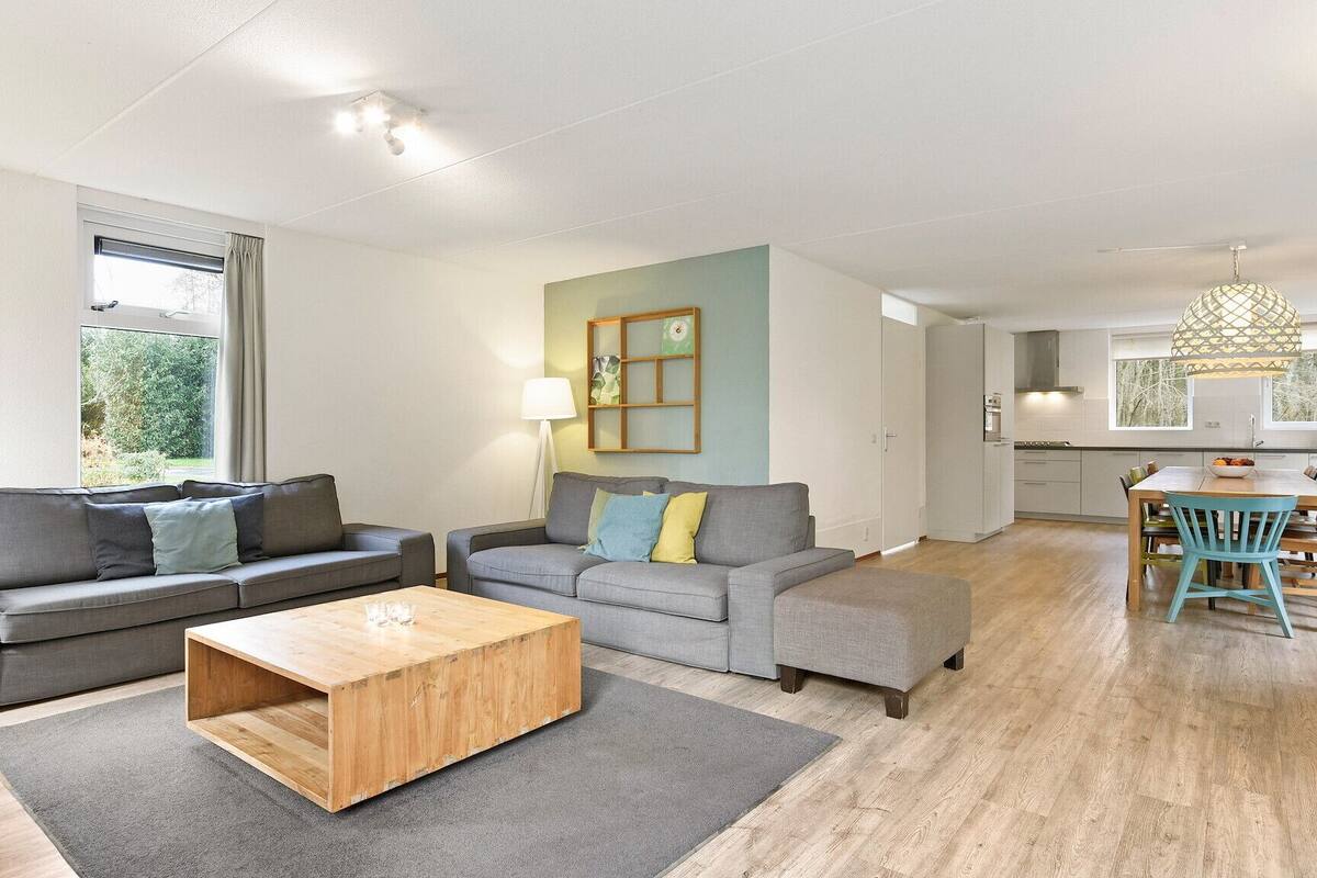 Un salon moderne avec deux canapés gris, une table basse en bois et un coin repas comprenant une table et des chaises en bois.