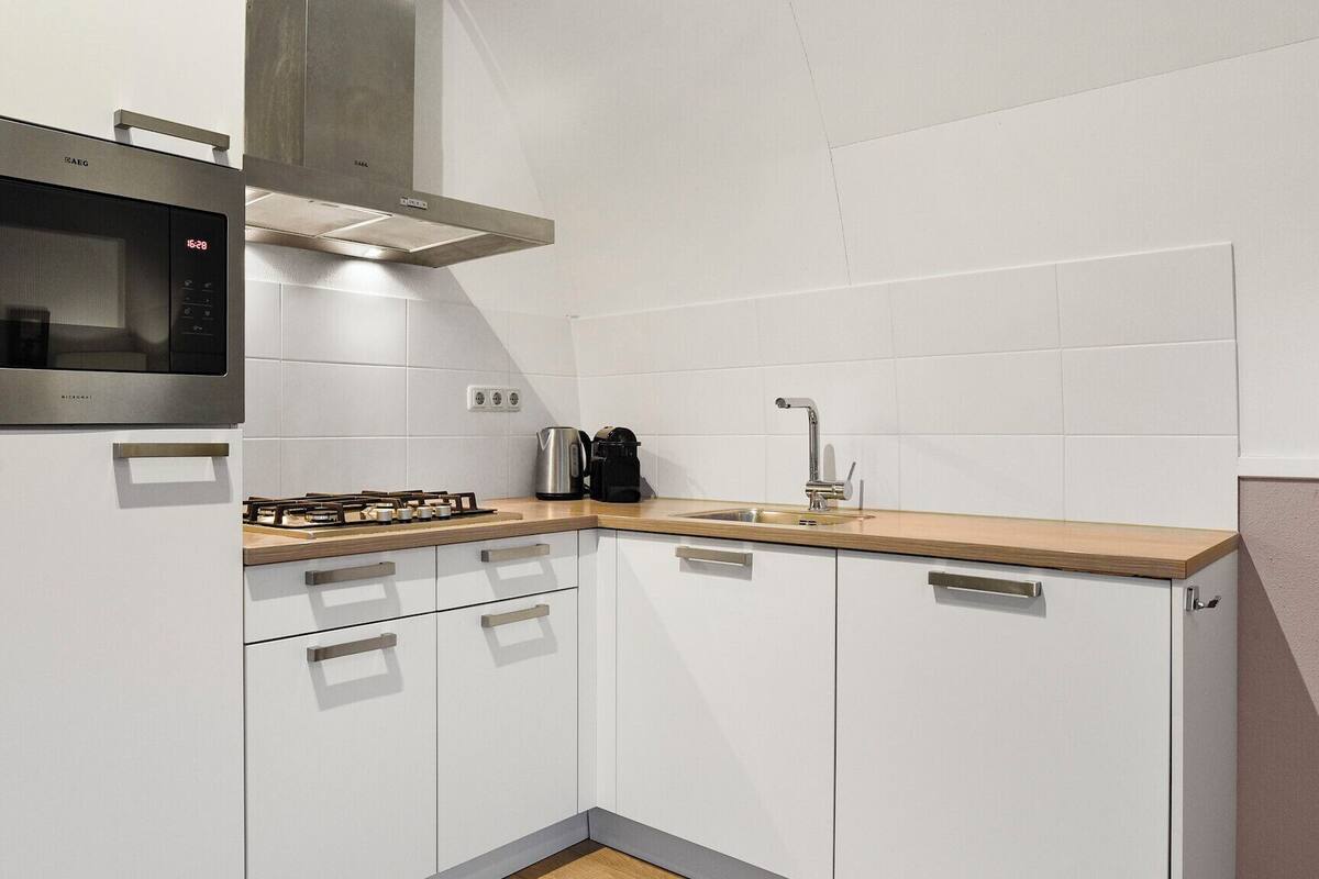 Une cuisine moderne avec des meubles blancs, un four à micro-ondes encastré, une cuisinière à gaz, une machine à café et un évier.