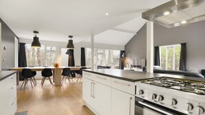 A modern kitchen with a central island, black chairs, a dining table, and a large window overlooking a garden. - Summio Waterpark De Bloemert (Midlaren)