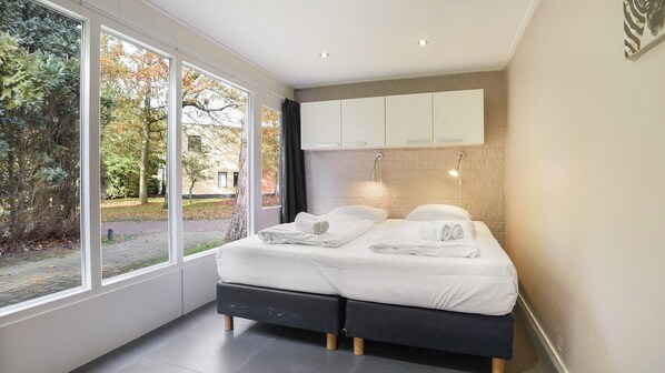 A modern bedroom with a large window, a bed with white linens, and a wall-mounted cabinet. - Summio Waterpark De Bloemert (Midlaren)