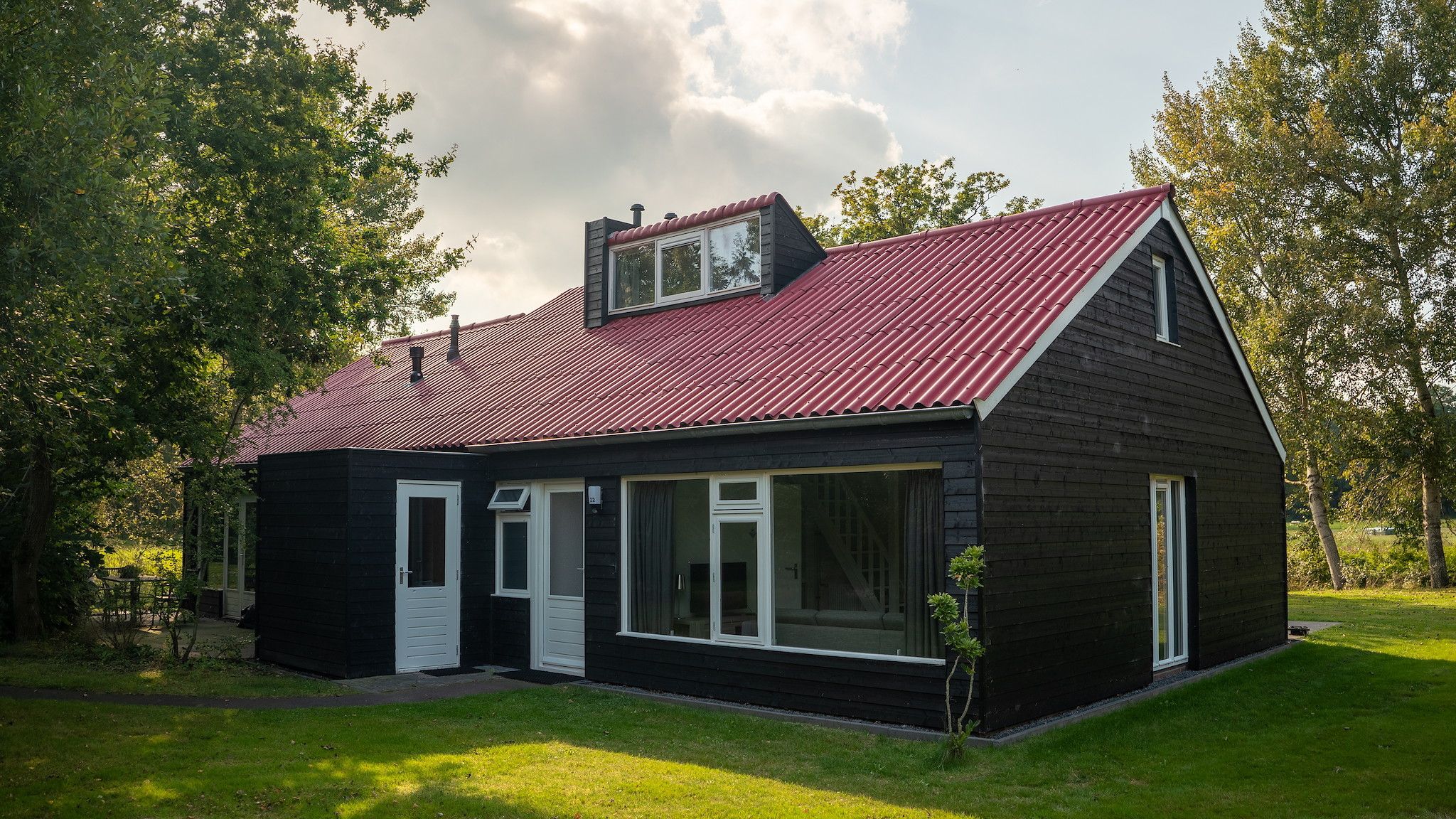 Una casa de madera negra con techo rojo, puertas blancas y ventanas grandes.