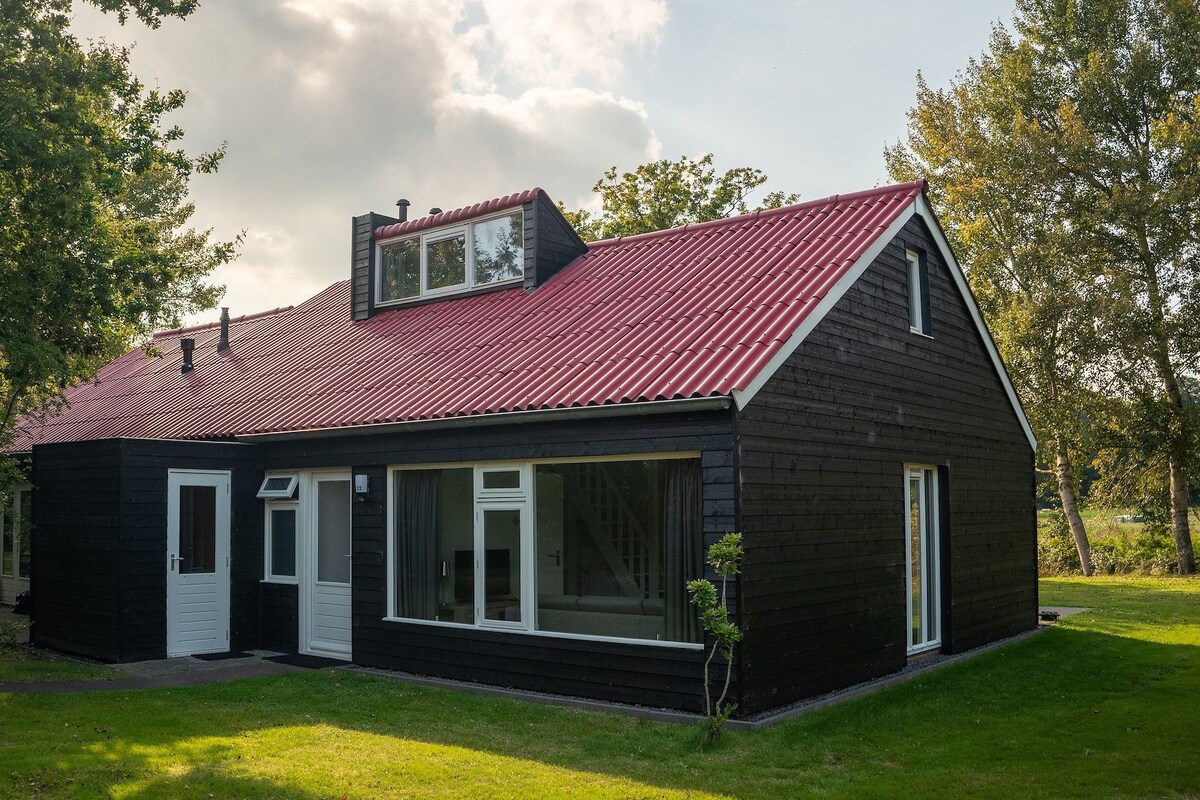 Une maison en bois peinte en noir, avec un toit rouge, des portes blanches et de grandes fenêtres.
