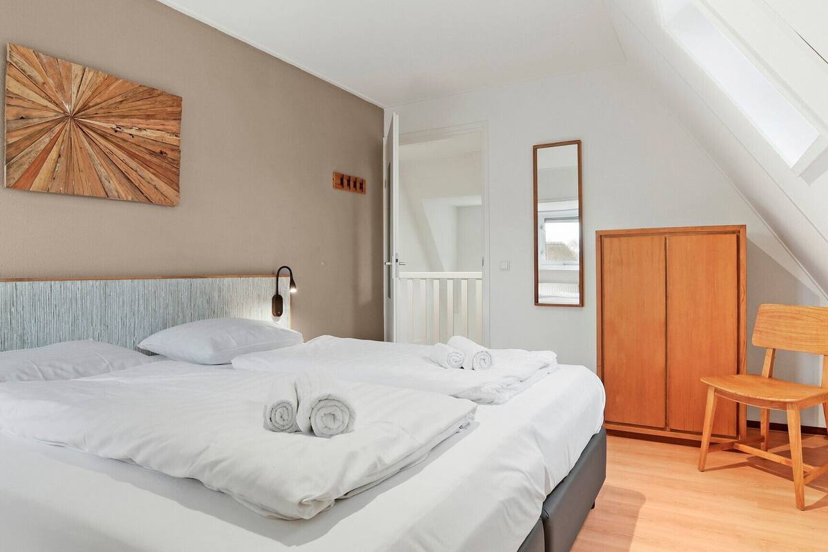 Une chambre à coucher comprenant un lit, une chaise en bois, une armoire et une œuvre d’art murale.