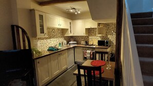 A compact kitchen with white cabinets, a microwave, and a toaster. A dining table with a red placemat and a chair is visible. - Cosy Cottage for two in the Centre of Sedbergh (Sedbergh)