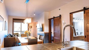Una cocina moderna con un lavamanos grande, zona de comedor con sillas y un televisor montado en la pared.