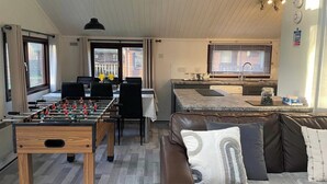 Una sala de estar acogedora con mesa de fútbol, sofá con cojines, comedor con mesa y sillas, y cocina con lavaplatos y encimera.