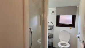 Un baño con cabina de ducha de vidrio, inodoro y ventana con persiana.