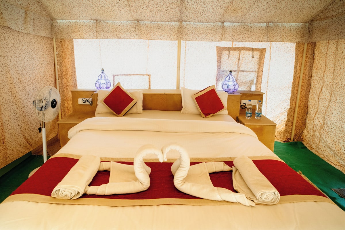 A hotel room with a large bed, two nightstands, a fan, and a window with curtains.