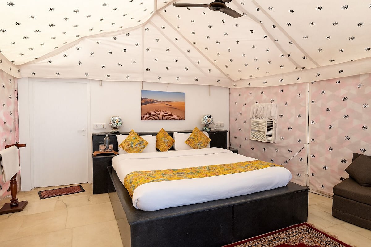 A bedroom with a bed, nightstands, a ceiling fan, a wall-mounted air conditioner, and a decorative rug.