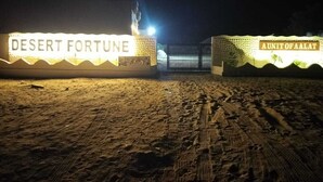 A nighttime view of a desert-themed entrance with illuminated signs reading "DESERT FORTUNE" and "AUNIFOFALAT". - Desert Fortune Resort (Jaisalmer)