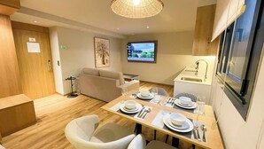 Quarto de hotel compacto com área de jantar, um sofá, televisão e uma pequena cozinha.