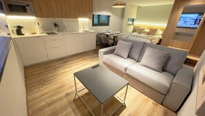 Quarto de hotel moderno com cozinha compacta, sofá, mesa pequena e televisão.