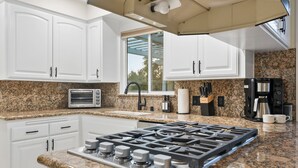 A modern kitchen with white cabinets, granite countertops, a built-in gas stove, a microwave, a coffee maker, and a window providing natural light.