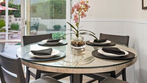 A round glass table with four chairs, a vase with flowers, and plates with napkins.
