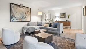 A modern living room with a grey sectional sofa, a coffee table, and a large abstract painting on the wall.