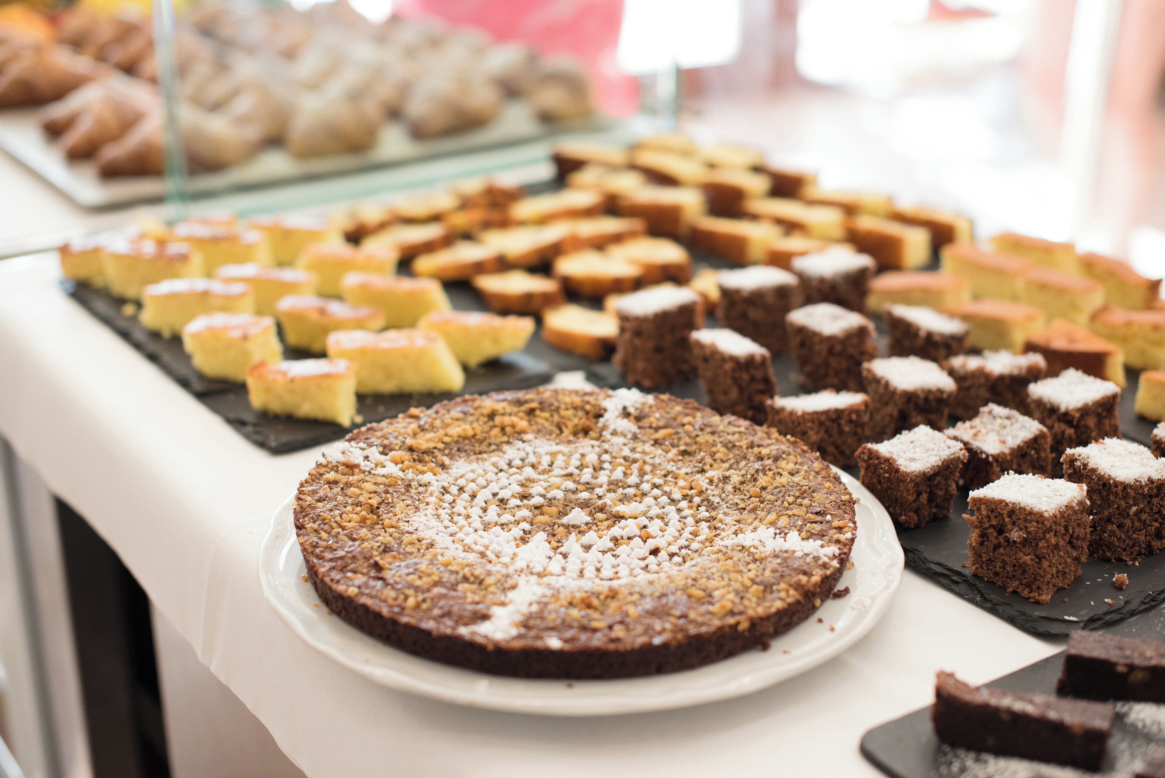 Variedad de postres a la vista, incluyendo un pastel grande y redondo, y varias porciones cuadradas.