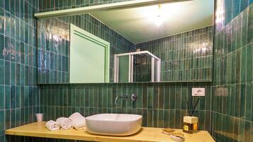 Un baño con un espejo grande, un tocador de madera, un lavamanos blanco y paredes cubiertas de azulejos verdes.