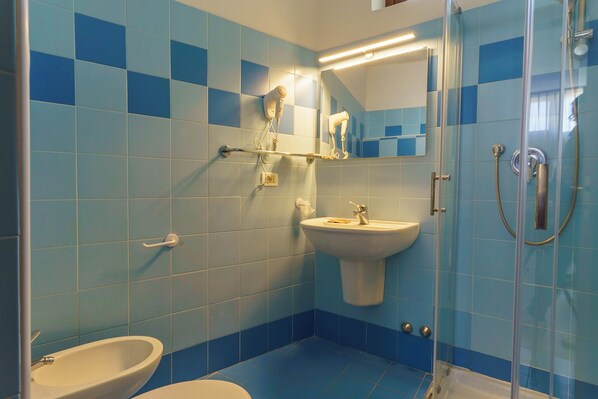Une salle de bain avec des carreaux bleus, un lavabo, un miroir, un sèche-mains et une douche.