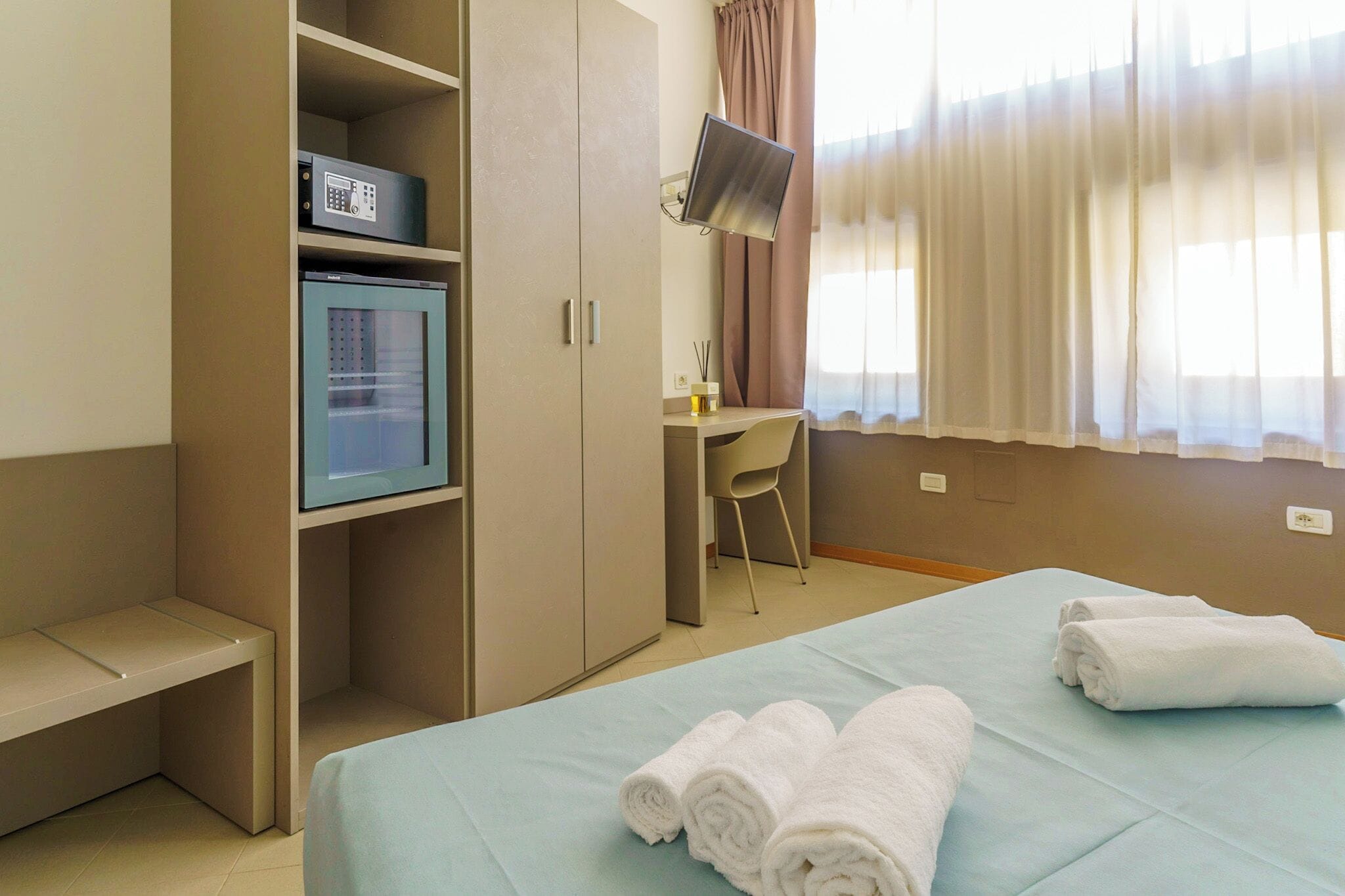 Een hotelkamer met een bed, een bureau, een stoel, een minibar en een televisie.