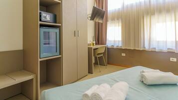 Een hotelkamer met een bed, een bureau, een stoel, een minibar en een televisie.