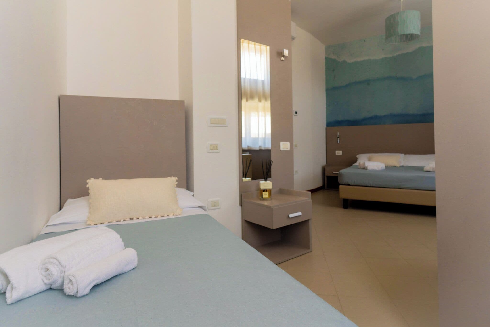 Ein Hotelzimmer mit Bett, Nachttisch, Spiegel und Wandgemälde.
