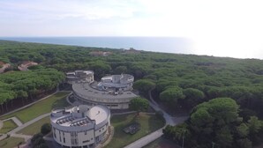 A circular building complex with multiple levels and a central courtyard, surrounded by dense greenery and a coastal view. - Csa Hotel Beach & Park (Bibbona)
