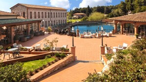 A courtyard with a swimming pool, outdoor seating, and a building with arched windows. - Csa Hotel Beach & Park (Bibbona)