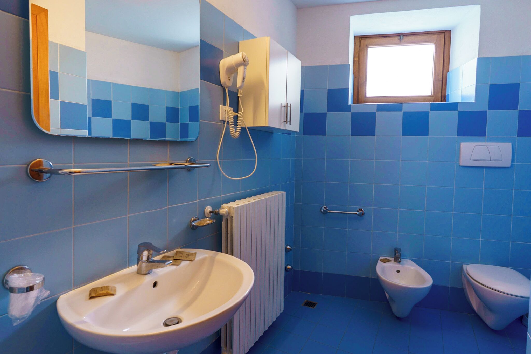 Un baño con lavamanos, bidé y secador de pelo fijado a la pared.