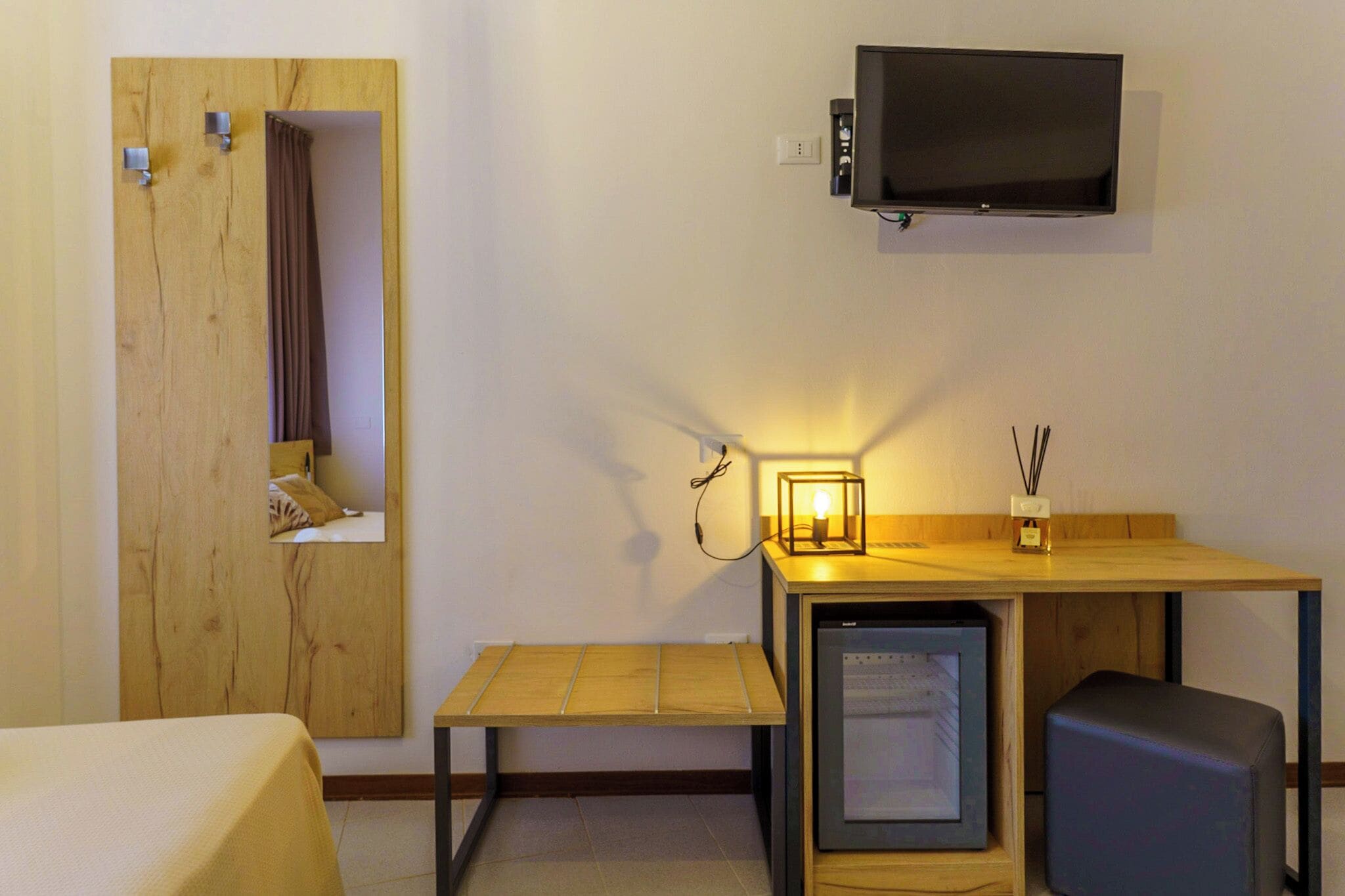 Una camera d'albergo compatta con un letto, una piccola scrivania con televisione, un mini-frigorifero e uno specchio.