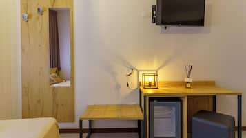 Una camera d'albergo compatta con un letto, una piccola scrivania con televisione, un mini-frigorifero e uno specchio.