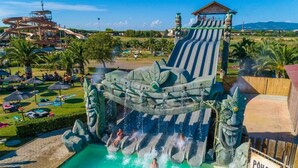 A water park with a large slide, a pool area, and palm trees. - Csa Hotel Beach & Park (Bibbona)