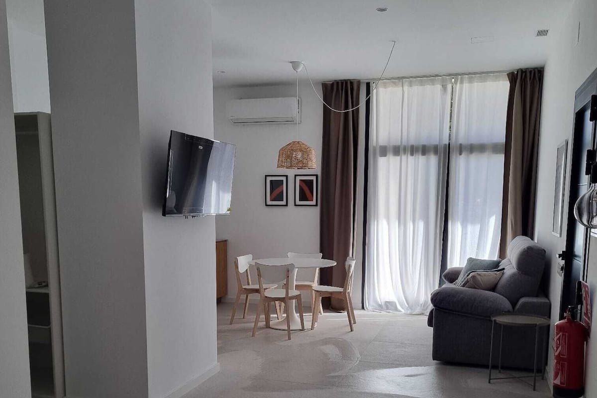 Une chambre d’hôtel moderne équipée d’un lit, d’un téléviseur fixé au mur, d’un coin repas avec une table et des chaises, et d’un canapé.