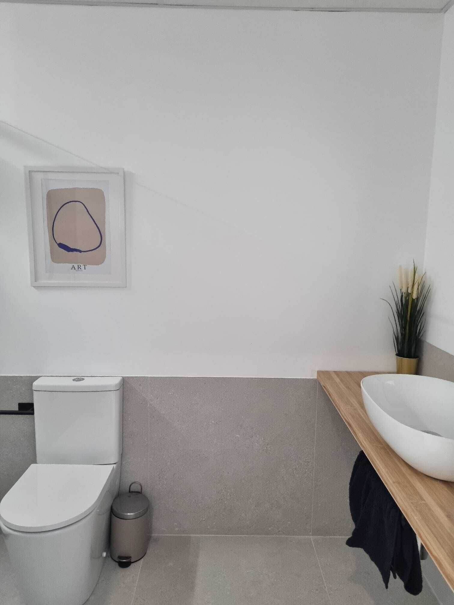 A modern bathroom with a toilet, trash can, and a sink on a wooden countertop.