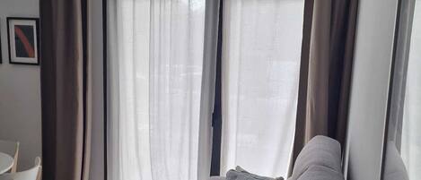 A living room with a grey sofa, a small table, and a window with sheer curtains.