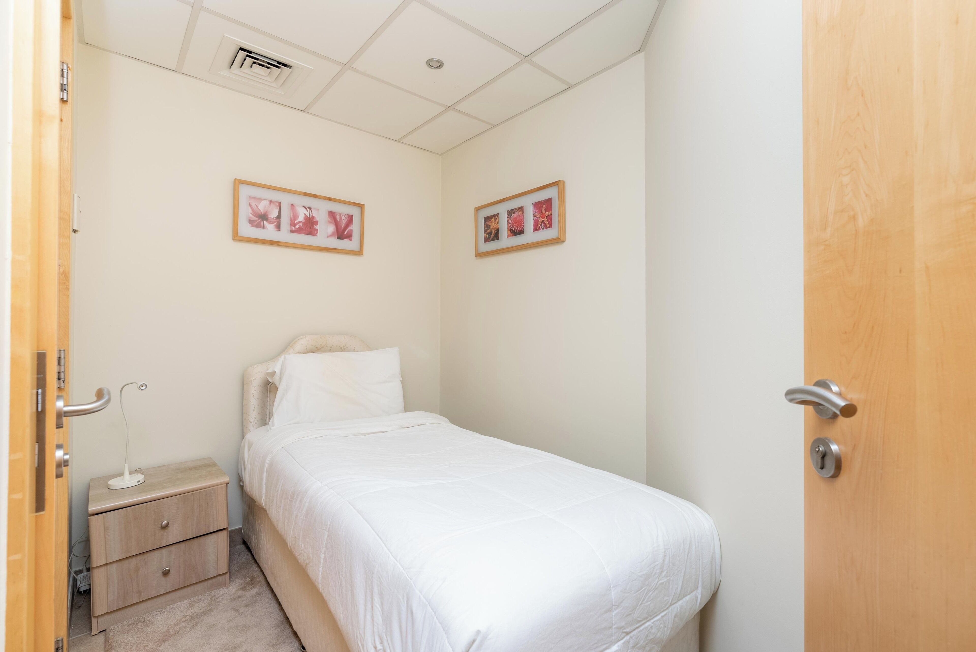 Een slaapkamer met een eenpersoonsbed, een nachtkastje, een houten deur en twee ingelijste foto's aan de muur.