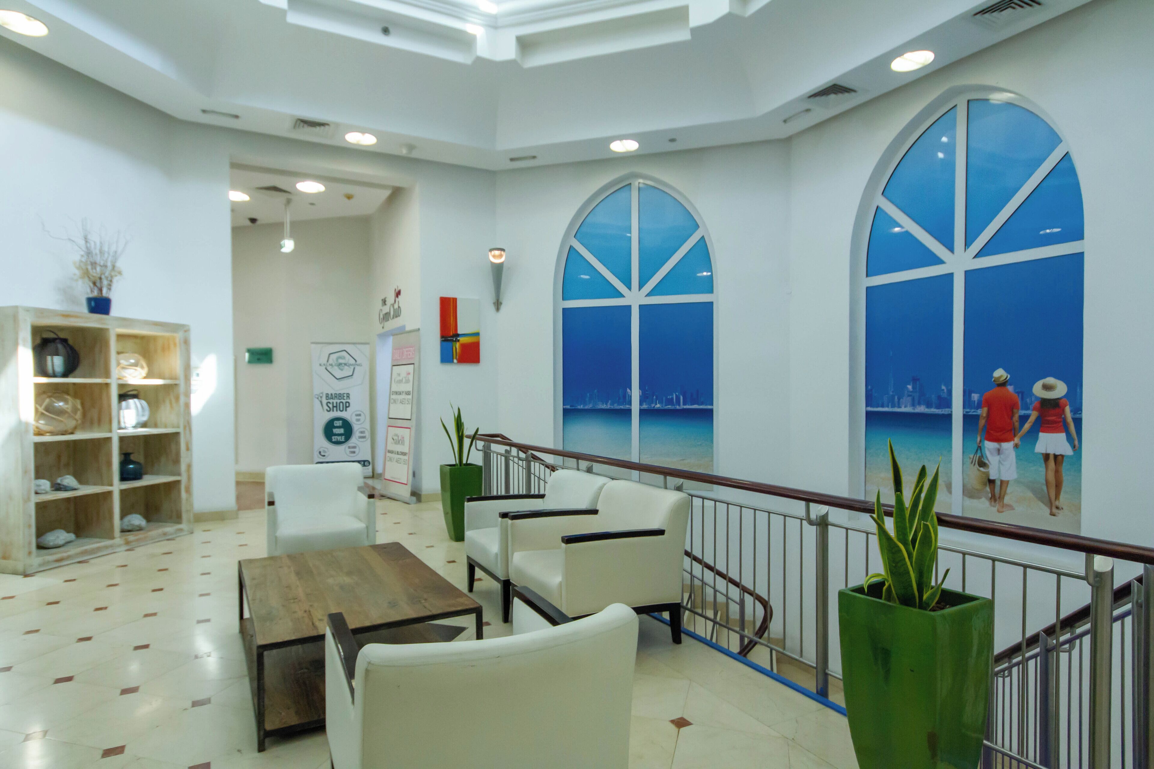 A spacious lobby with a wooden coffee table, white armchairs, and a large window with a cityscape view.