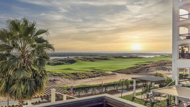 A view of a golf course with a palm tree and a building with balconies. - Cozy Golfside Studio (Abu Dhabi)