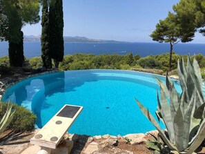 Una piscina circular con agua cristalina y azul, rodeada de follaje y con vistas a una extensión de agua.