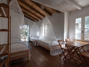 Una habitación con dos camas cubiertas por mosquiteros blancos, una mesa de madera y sillas.