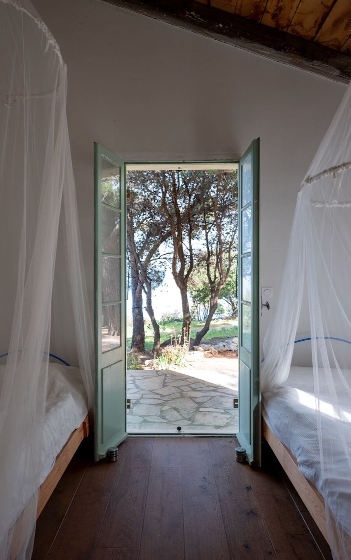 Habitación con cama bajo un dosel, una puerta que da a un espacio exterior con árboles y un sendero de piedra.