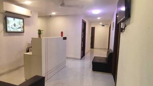Een hotel receptie met een receptiebalie, een aan de muur bevestigde televisie en een zithoek met een bank.