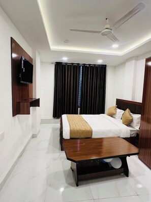 Une chambre d’hôtel équipée d’un lit, d’une table de chevet, d’un téléviseur fixé au mur et d’un ventilateur de plafond.