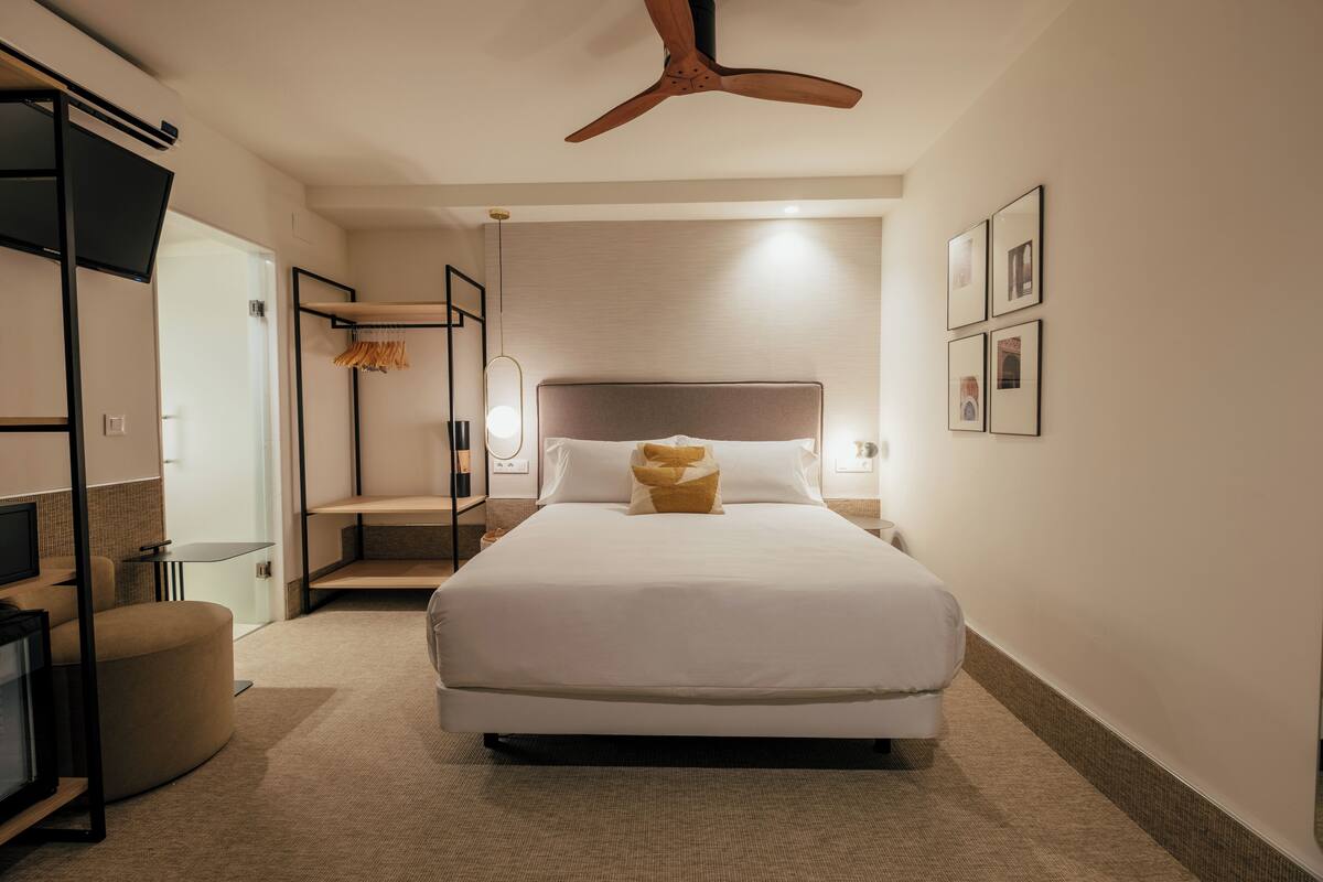 Une chambre d’hôtel moderne dotée d’un grand lit, d’un ventilateur de plafond, d’une télévision et d’un coin salon.
