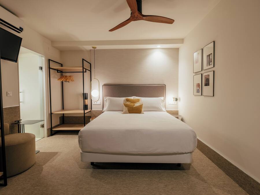 A modern hotel room with a large bed, a ceiling fan, a TV, and a seating area.