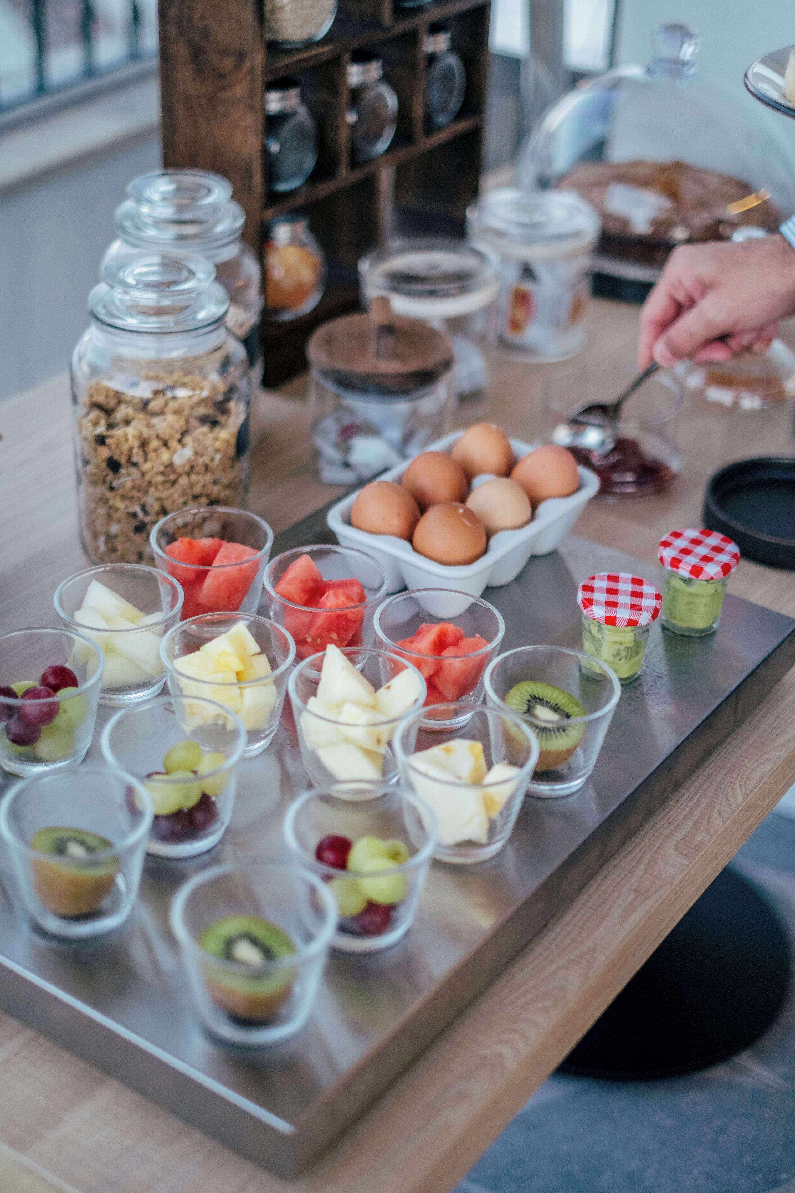 A breakfast buffet with various fruits, eggs, and granola.